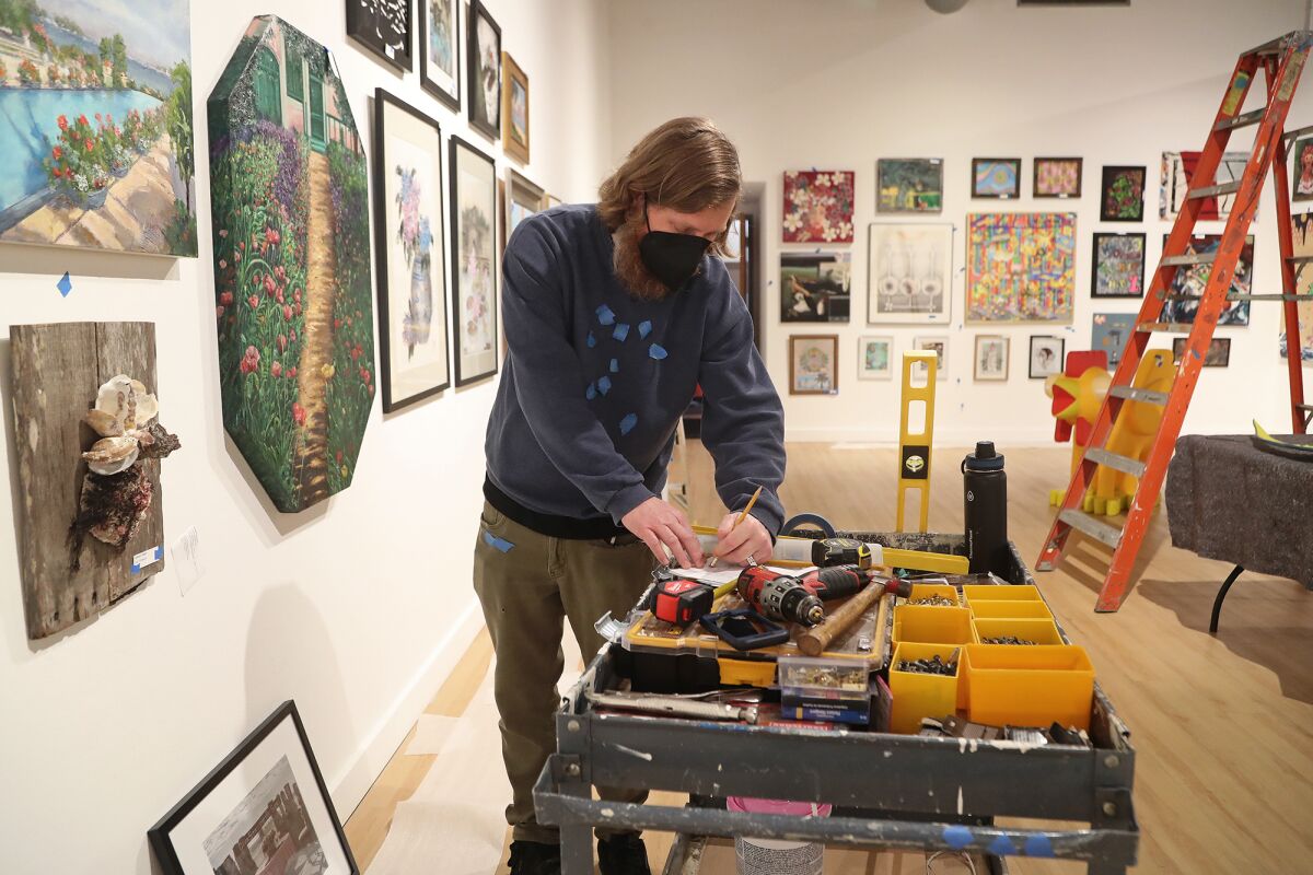 Preparator Eamonn Swiftfox goes over his notes as he hangs up art pieces in preparation for Centered on the Center.