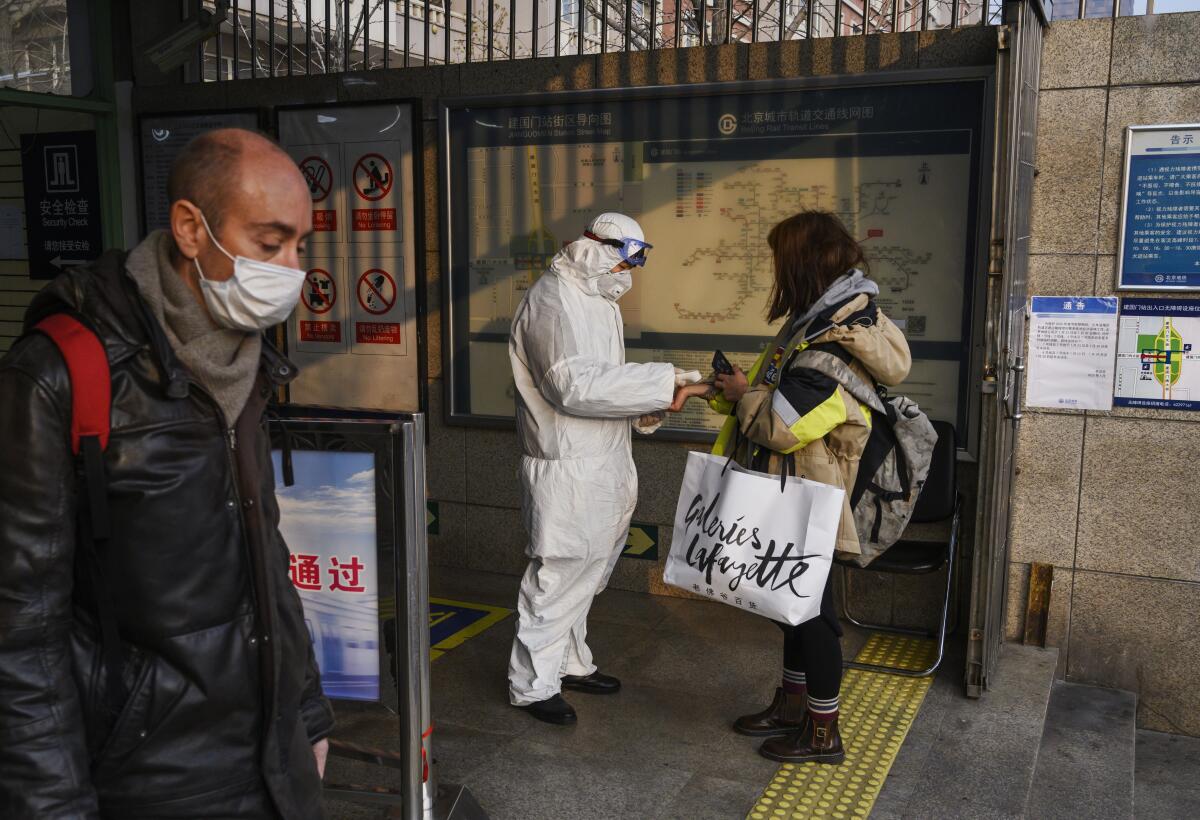 A health worker in a protective suit takes the temperature of a woman at a subway station in Beijing on Jan. 28.