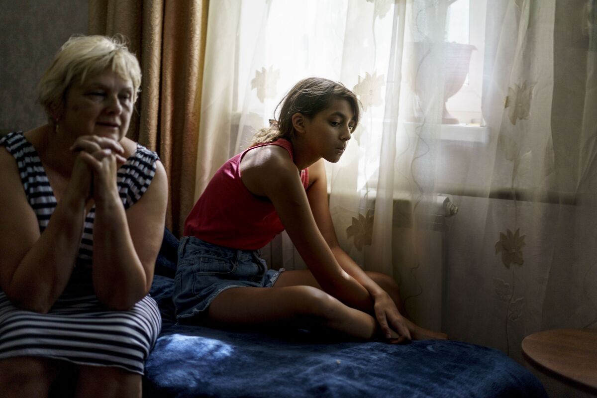 Anastasiia Aleksandrova, 12, right, sits with her grandmother, Olena, at their home in Sloviansk, Donetsk region, eastern Ukraine, Monday, Aug. 8, 2022. With cities largely emptied after hundreds of thousands have evacuated to safety, the young people that remain face alienation, loneliness and boredom as unlikely yet painful counterpoints to the fear and violence Moscow has unleashed on Ukraine. (AP Photo/David Goldman)