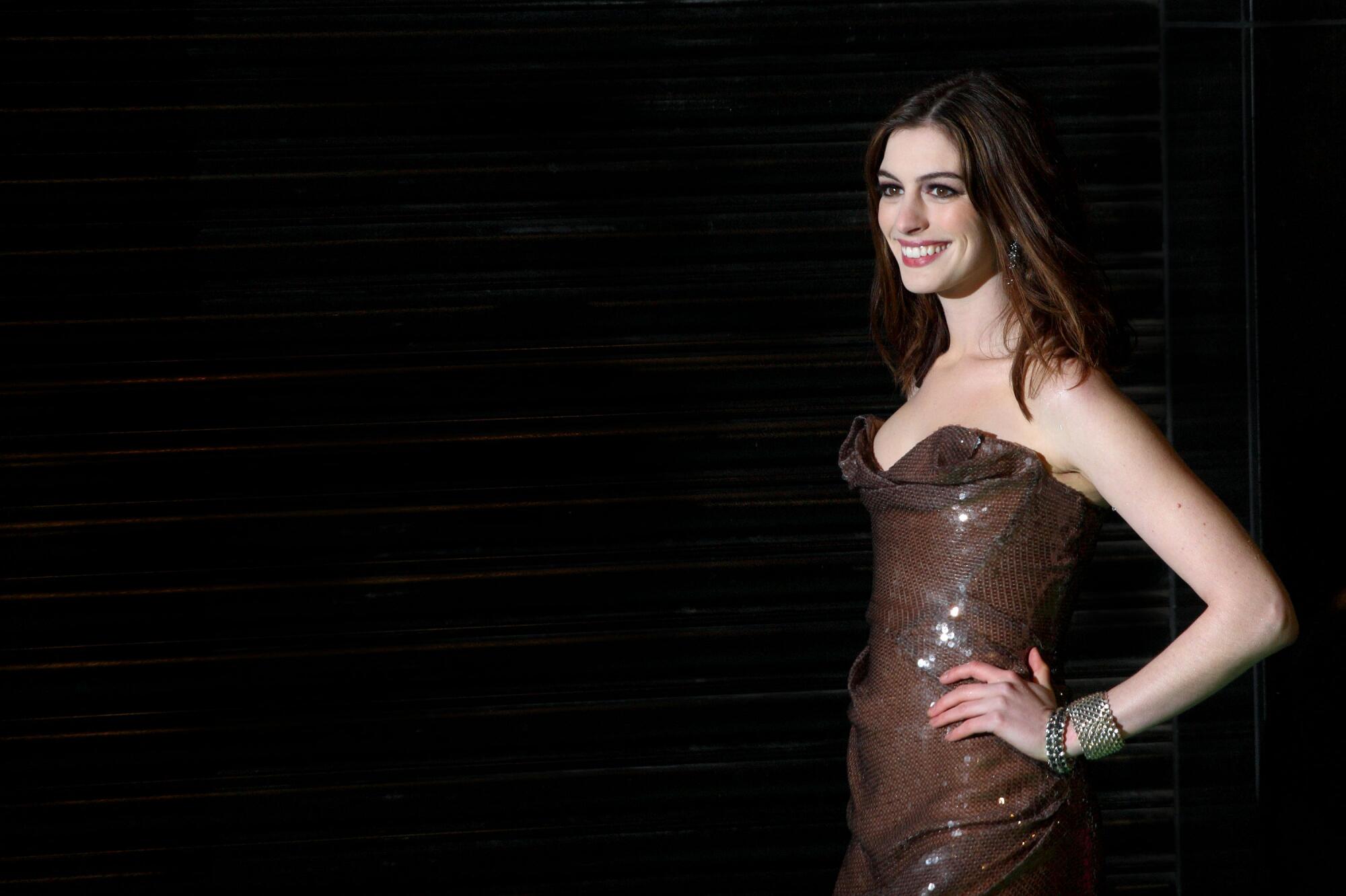 A smiling dark-haired woman shows off her brown gown.