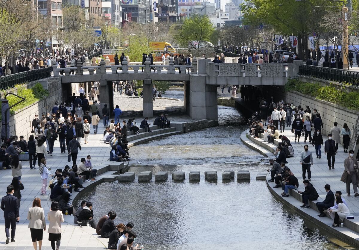 People wearing face masks walk along the public area of the Cheonggye Stream in Seoul, South Korea, Friday, April 15, 2022. South Korea will remove most pandemic restrictions, including indoor gathering limits, as it slowly wiggles out of an omicron outbreak officials say is stabilizing. (AP Photo/Ahn Young-joon)