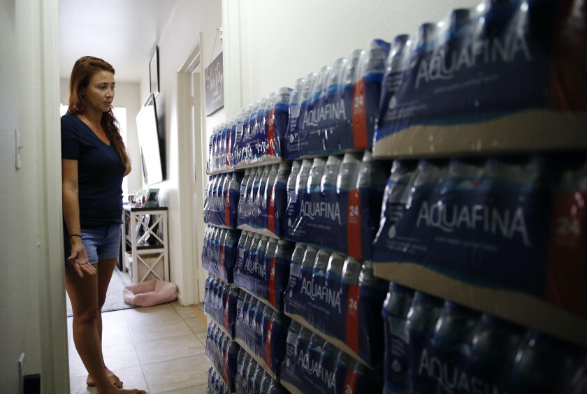 Lauren Wright, a Navy spouse whose family was sickened by jet fuel in their tap water, shows her supply of bottled water at her home in Honolulu, Friday, July 1, 2022. A Navy investigation says shoddy management and human error caused fuel to leak into Pearl Harbor's tap water last year. The leak poisoned thousands of people and forced military families to evacuate their homes for hotels. (AP Photo/Caleb Jones)