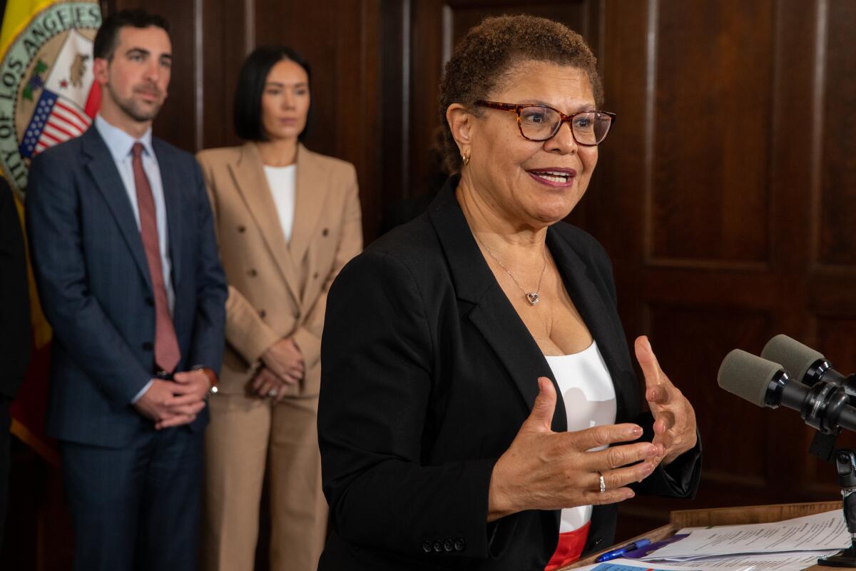 Mayor Karen Bass stands in front of two advisors at a podium.