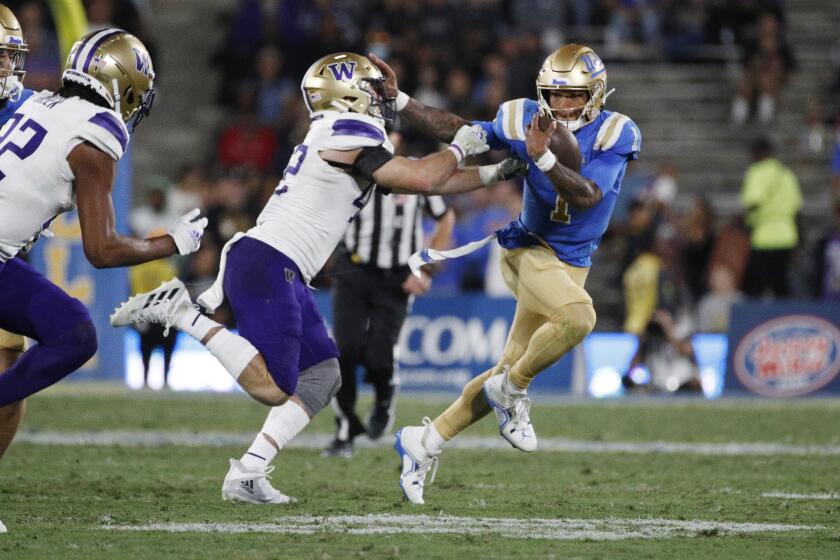 UCLA quarterback Dorian Thompson-Robinson stiff arms Washington safety Makell Esteen while running with the football