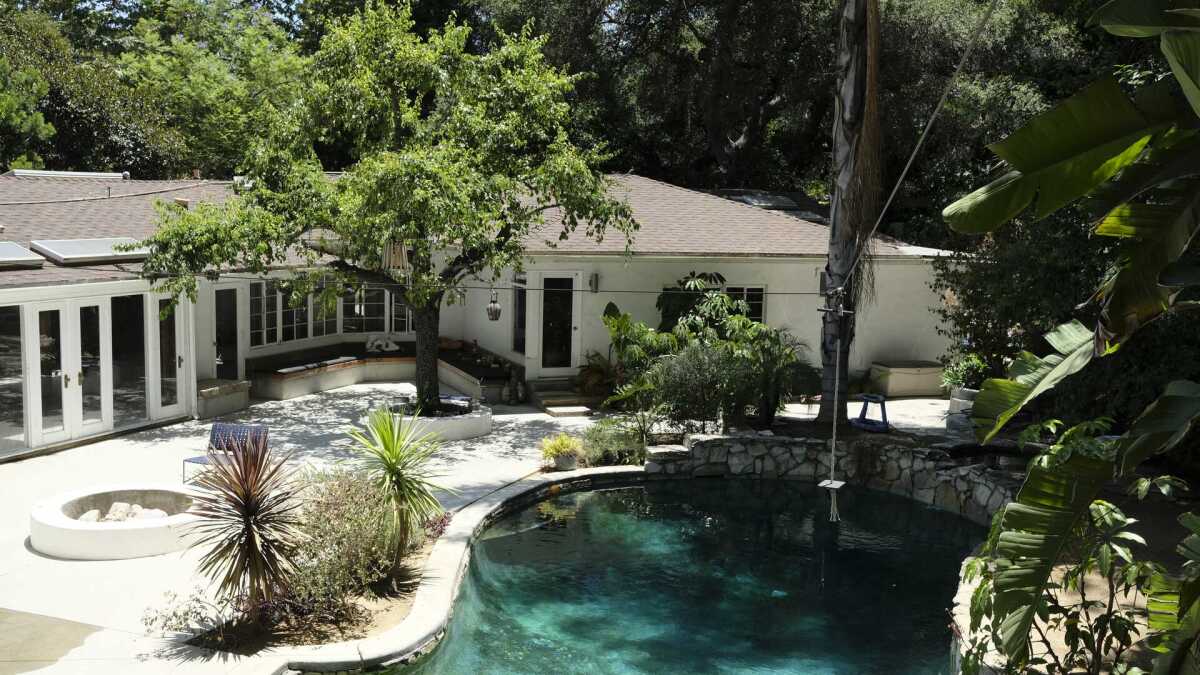 The back patio of a home with a fire pit, tall trees and a lagoon-style pool.