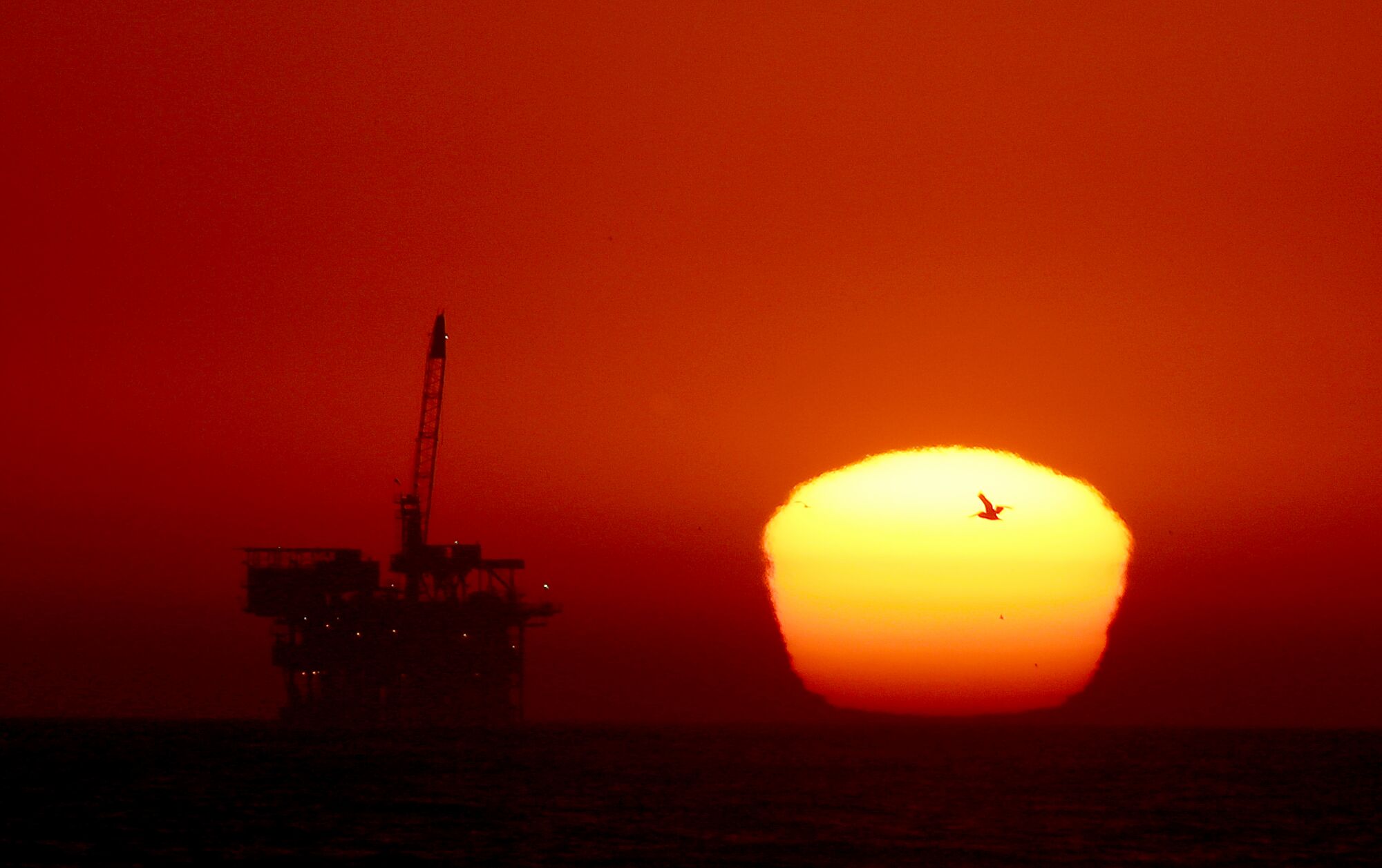The sun sets behind an oil drilling platform off the coast of Huntington Beach on Monday.