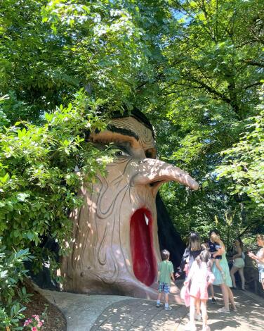 A giant witch face in a forest surrounded by real children looking on.