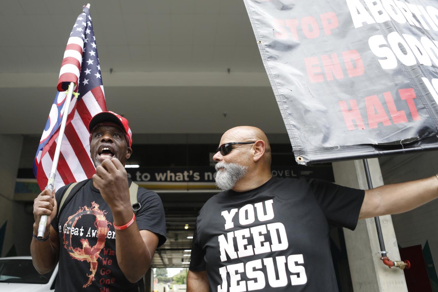 A person holding a sign talks to a person holding a U.S. flag