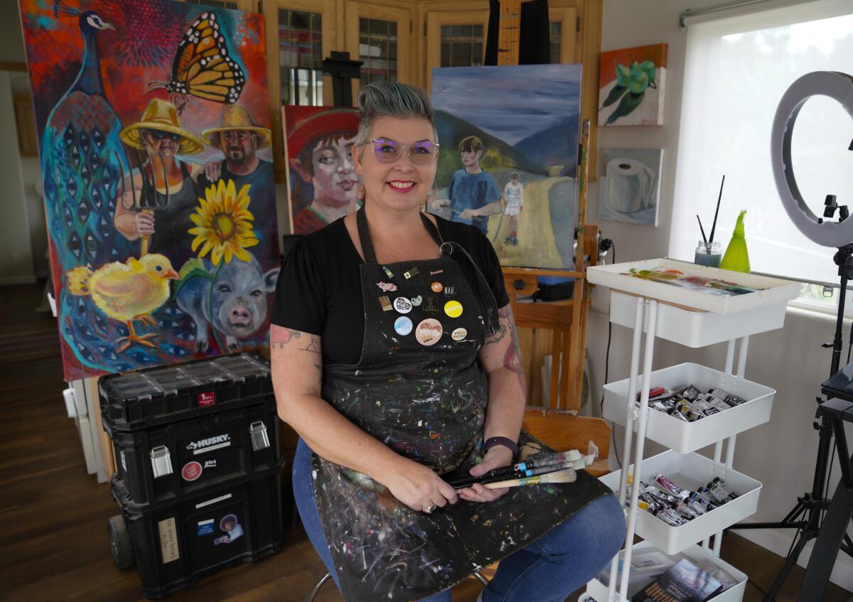 Artist Wendy Kwasny at her home art studio wearing a black smock covered in paint splatter