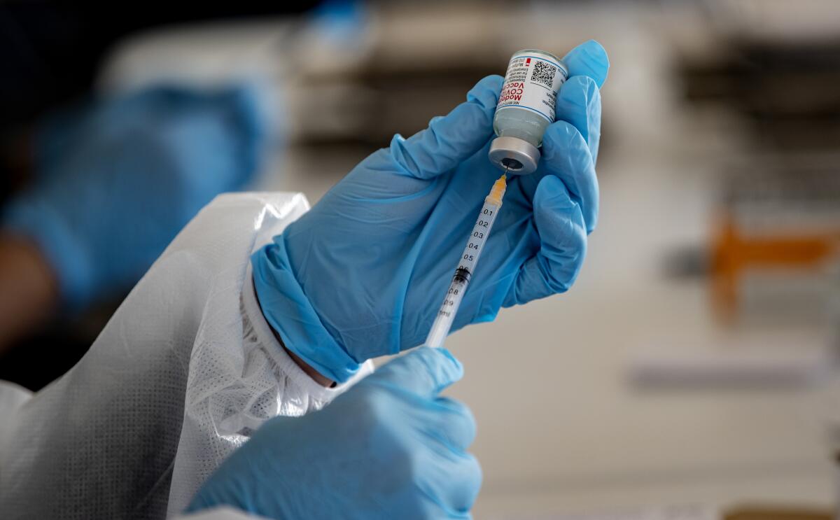 A healthcare professional inserts a syringe into a vial of the Moderna vaccine