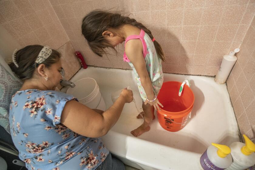 MADERA, CA - AUGUST 05, 2021: Sandra Sevilla, 45, washes the feet of her daughter Arianna, 5, inside a bathtub at their home in Madera. Now, the water is flowing out of the faucet at full speed thanks to a 2500 gallon water tank that was installed in the backyard of their home in Madera. In the past, they used buckets to catch any excess water dripping off the faucet. (Mel Melcon / Los Angeles Times).