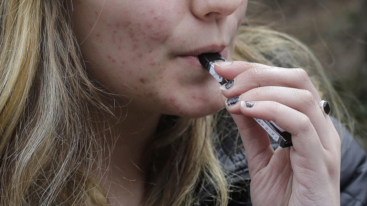 An unidentified 15-year-old high school student uses a vaping device near her school's campus in Cambridge, Mass.