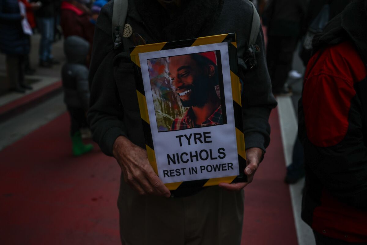 People gather to protest police violence. One person holds an image of Tyre Nichols with his name and 'rest in power'