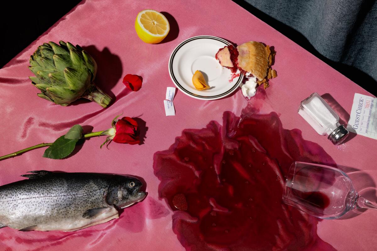 A table with a whole fish, artichoke, half a lemon, a rose and spilled red wine