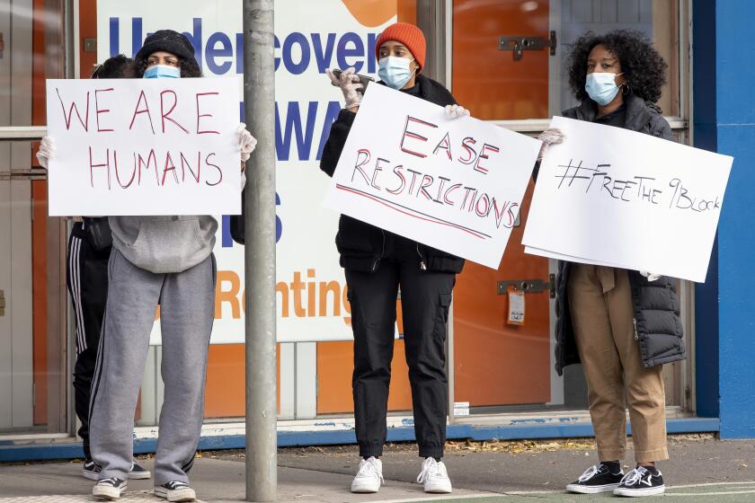 Women hold signs outside housing commission apartments under lockdown in Melbourne, Australia, on Monday, July 6, 2020. The leader of Australia’s most populous state says her government’s decision to close its border with hard-hit Victoria state marks a new phase in the country’s coronavirus pandemic. (AP Photo/Andy Brownbill)