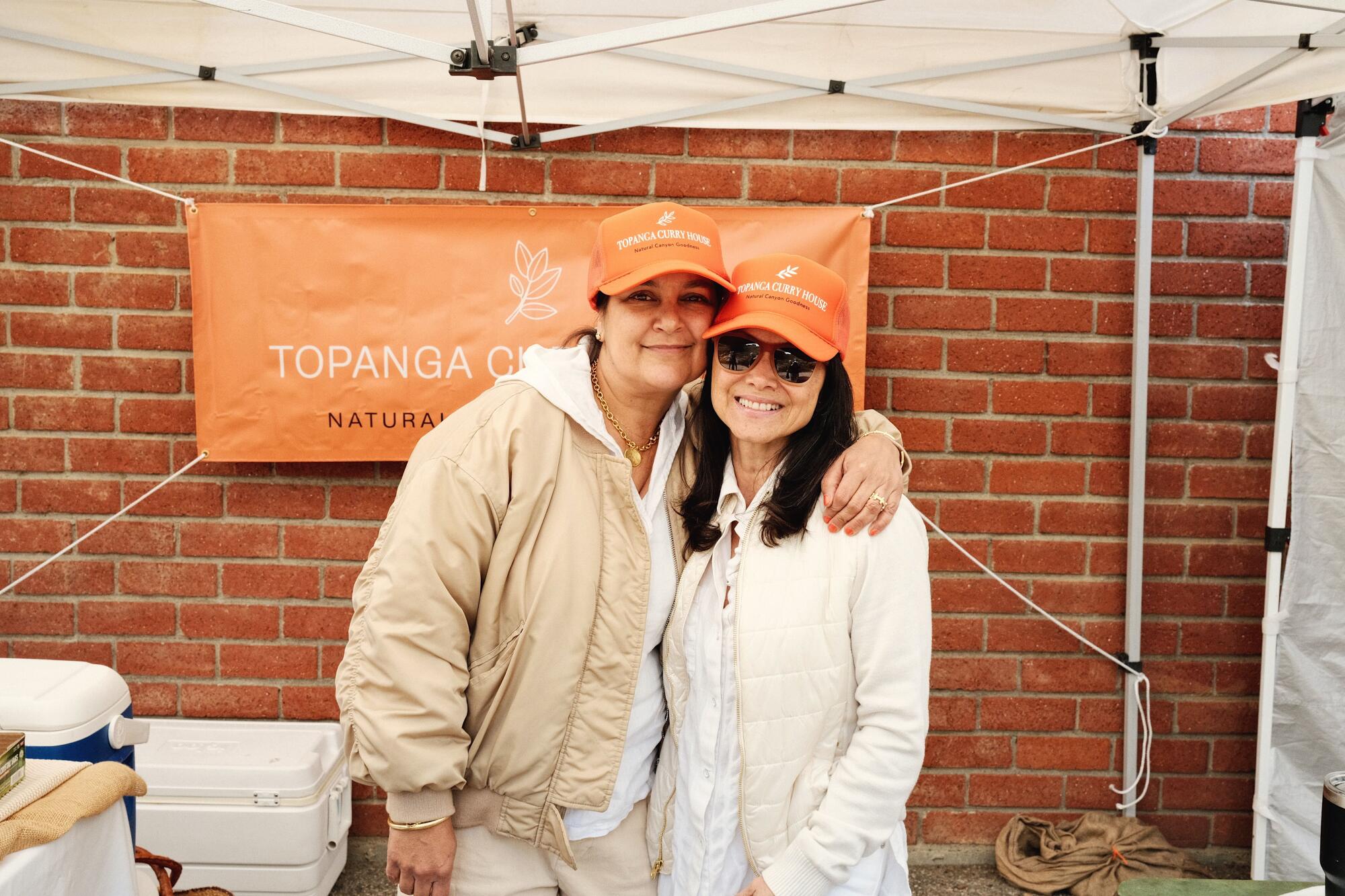 Claudia Joshi, left, with an arm around Destiny London at their orange-tended Topanga Curry House stall