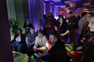 People wearing lanyards sit around a screen.