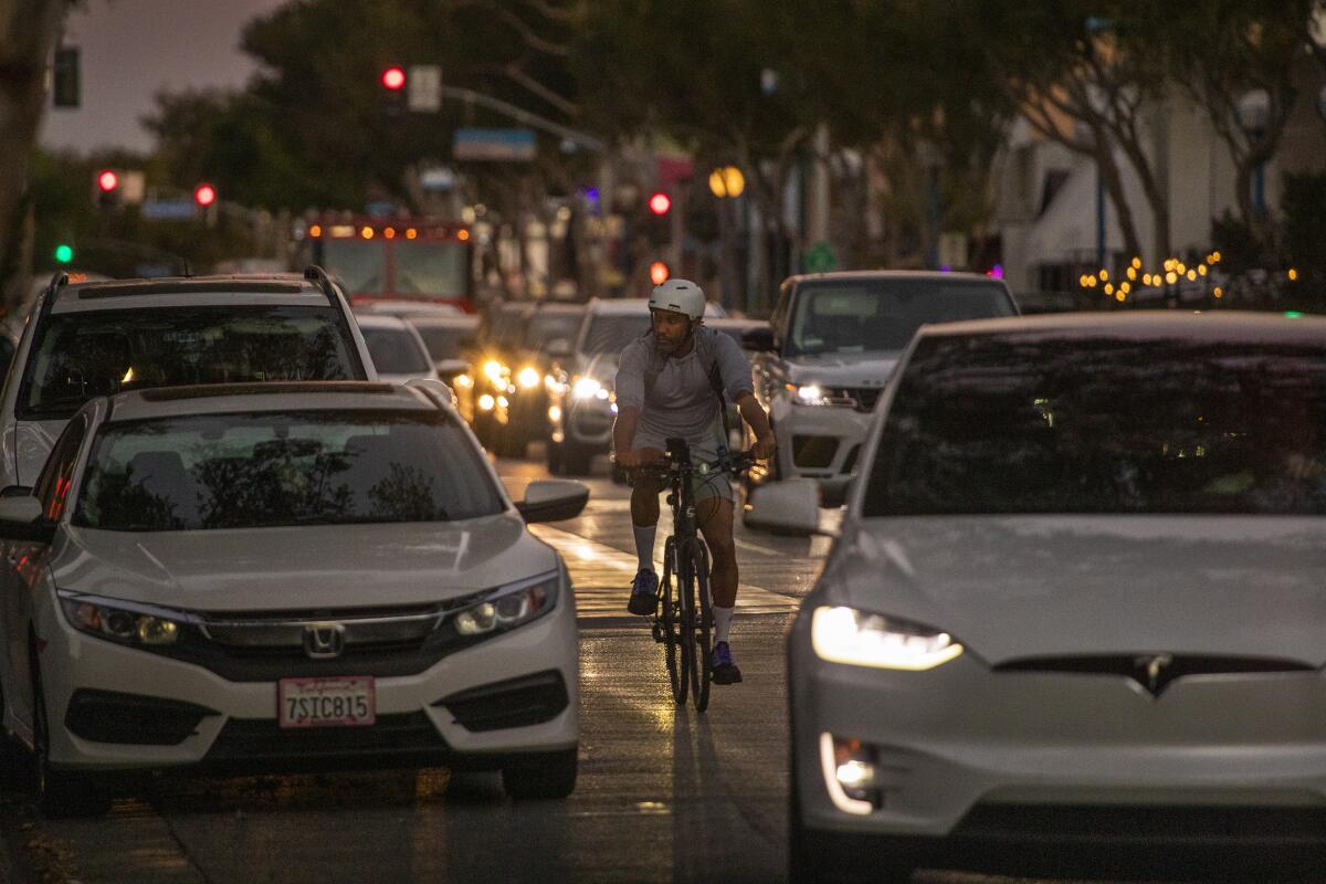 A person on a bike rides in traffic along at dusk.