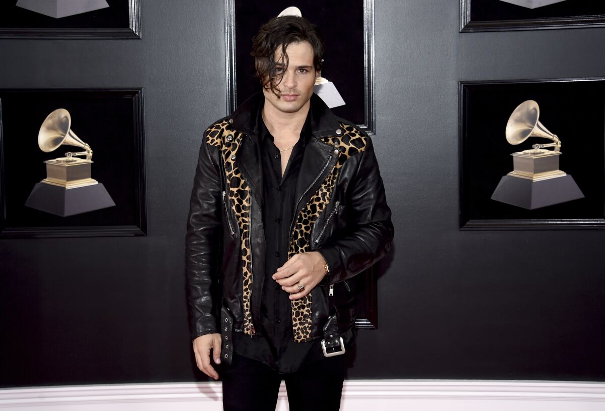A man in a black-and-leopard leather jacket stares ahead on an awards show red carpet