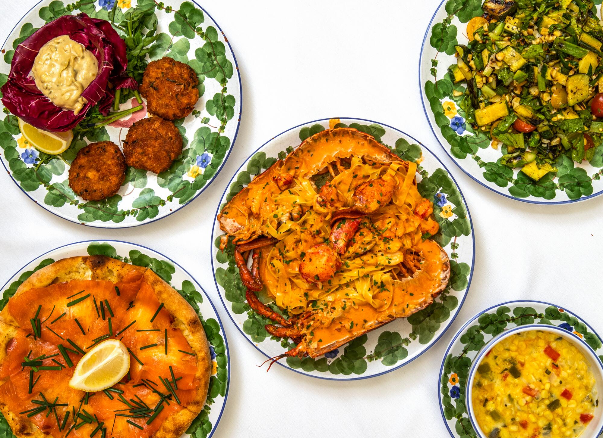 An array of dishes on plates decorated with green leafy motifs.