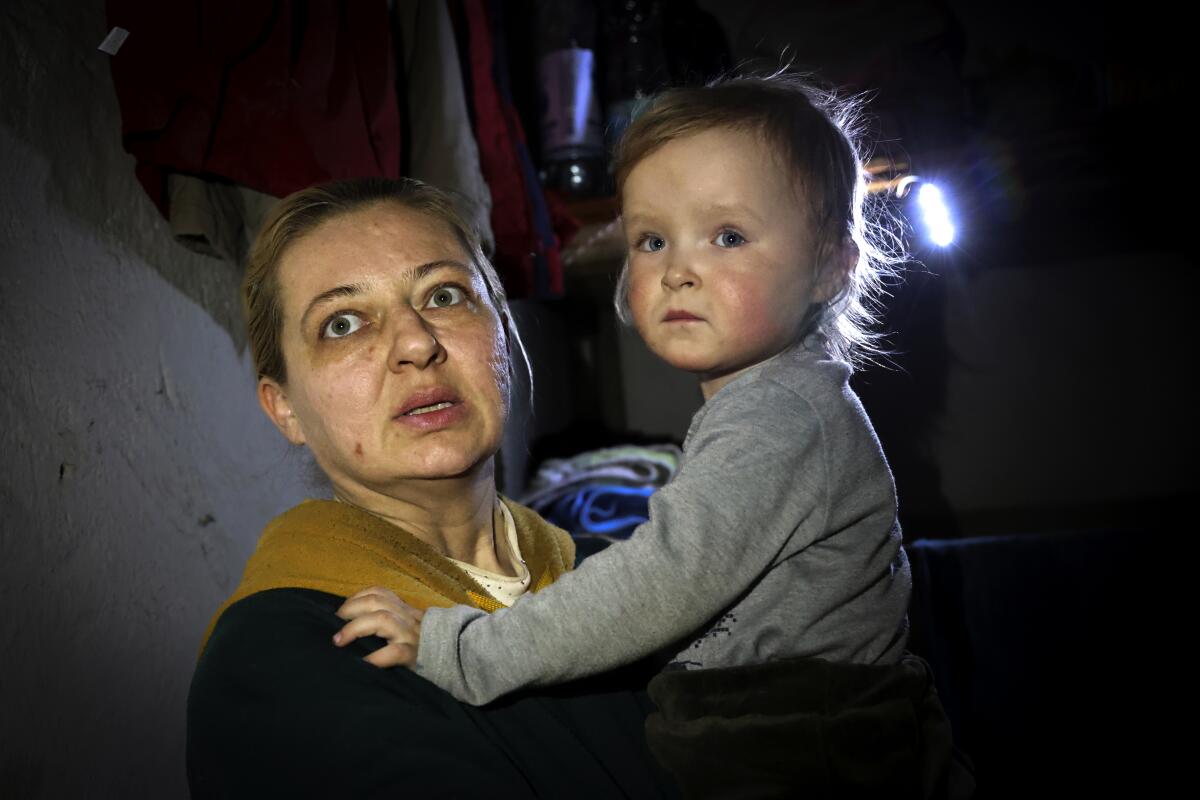 A wide-eyed woman in a dark basement holds a baby.