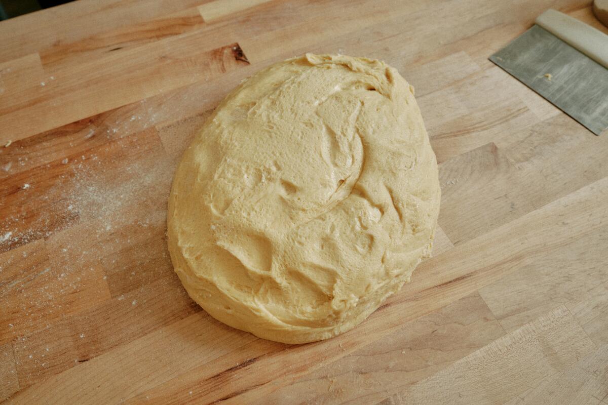 The dough for a pan de muerto rests on a floured wooden surface