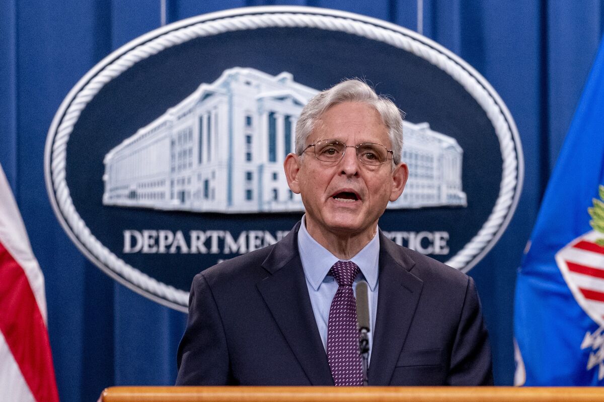Attorney General Merrick Garland stands in front of a Department of Justice logo. 