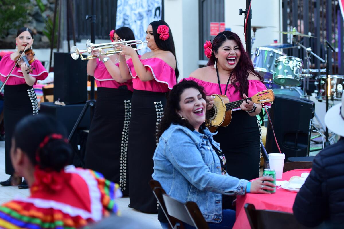 A female mariachi band plays music around people seated at tables.