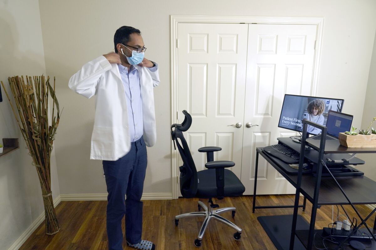 FILE - Medical director of Doctor on Demand Dr. Vibin Roy prepares to conduct an online visit with a patient from his work station at home, April 23, 2021, in Keller, Texas. Comfort levels with remote care can vary depending on factors like age, income level or race, according to the survey from The Associated Press-NORC Center for Public Affairs Research. (AP Photo/LM Otero, File)