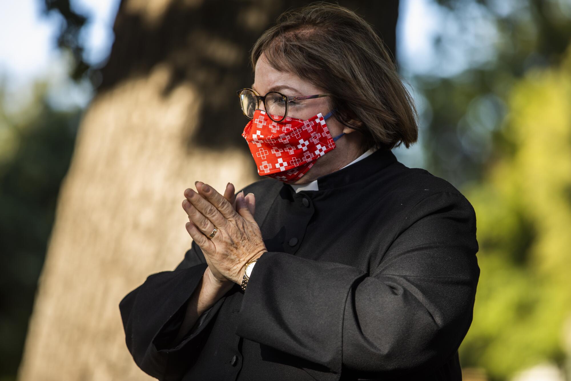 A woman in a face mask holds hands together.