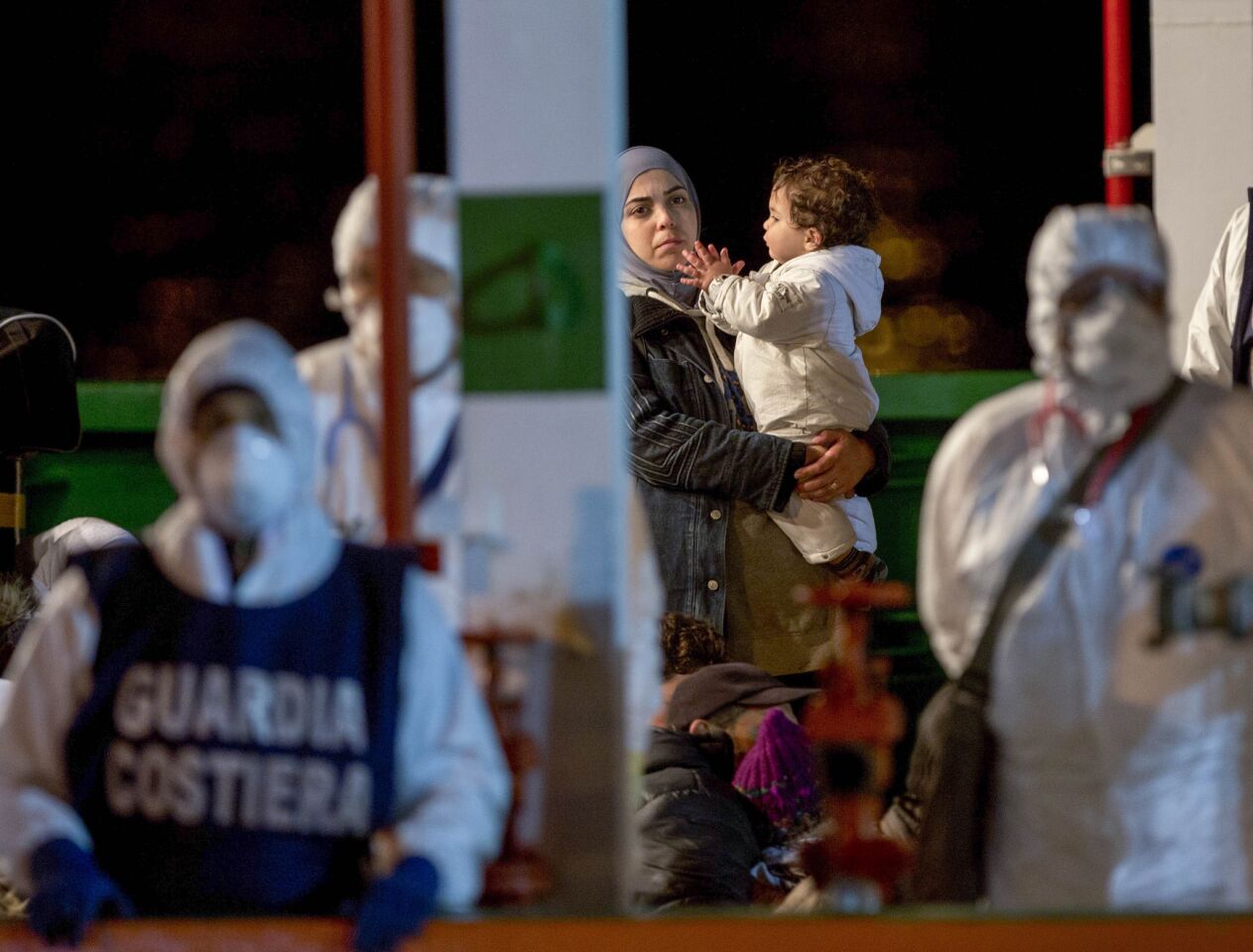 A woman carries a child as she disembarks in the Sicilian harbor of Pozzallo, Italy. About 100 migrants, including 28 children, were rescued on Sunday by a merchant vessel in the Sicilian Strait while they were trying to cross. Another smuggler's boat crammed with hundreds of people overturned off Libya's coast on Saturday as rescuers approached.