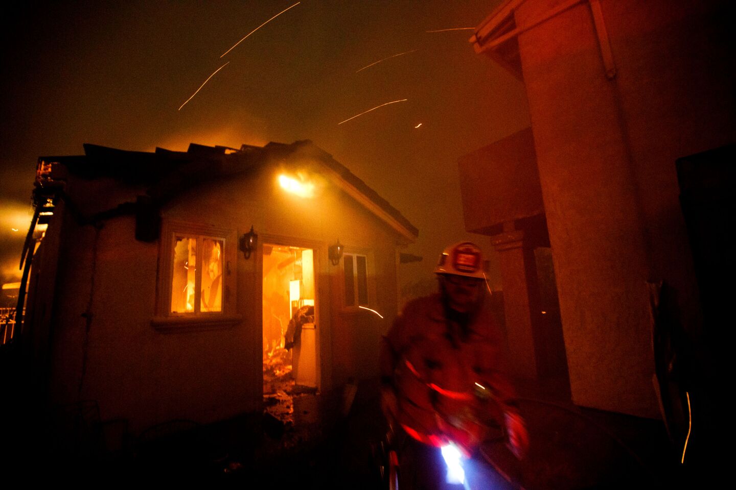 A firefighter works to contain the Saddleridge fire from spreading as structures burn in Porter Ranch.
