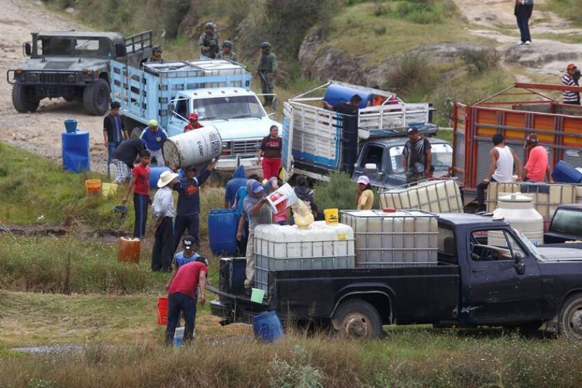 Fotografía de pobladores que llenan grandes bidones de combustible de una toma clandestina ante la mirada de elementos del Ejercito Mexicano. EFE/Archivo