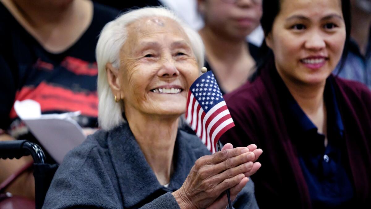 Hong Inh smiles and waves an American flag after taking the oath to become a United States citizen at the Los Angeles Convention Center on Tuesday. At 103, the Cambodian woman was the oldest of more than 10,000 people who took the oath of allegiance.