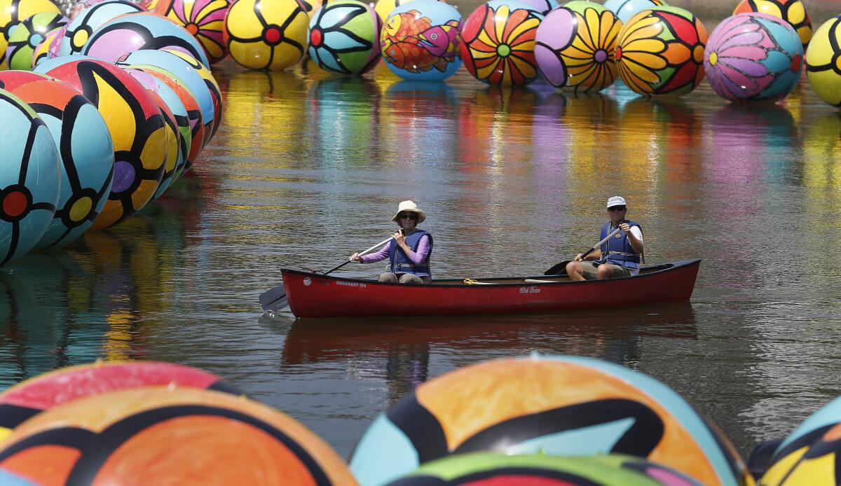 The public art project "Spheres at MacArthur Park" is covering the park's lake in a sea of colorful balls. Two volunteers paddle their way through the installation on Saturday morning.