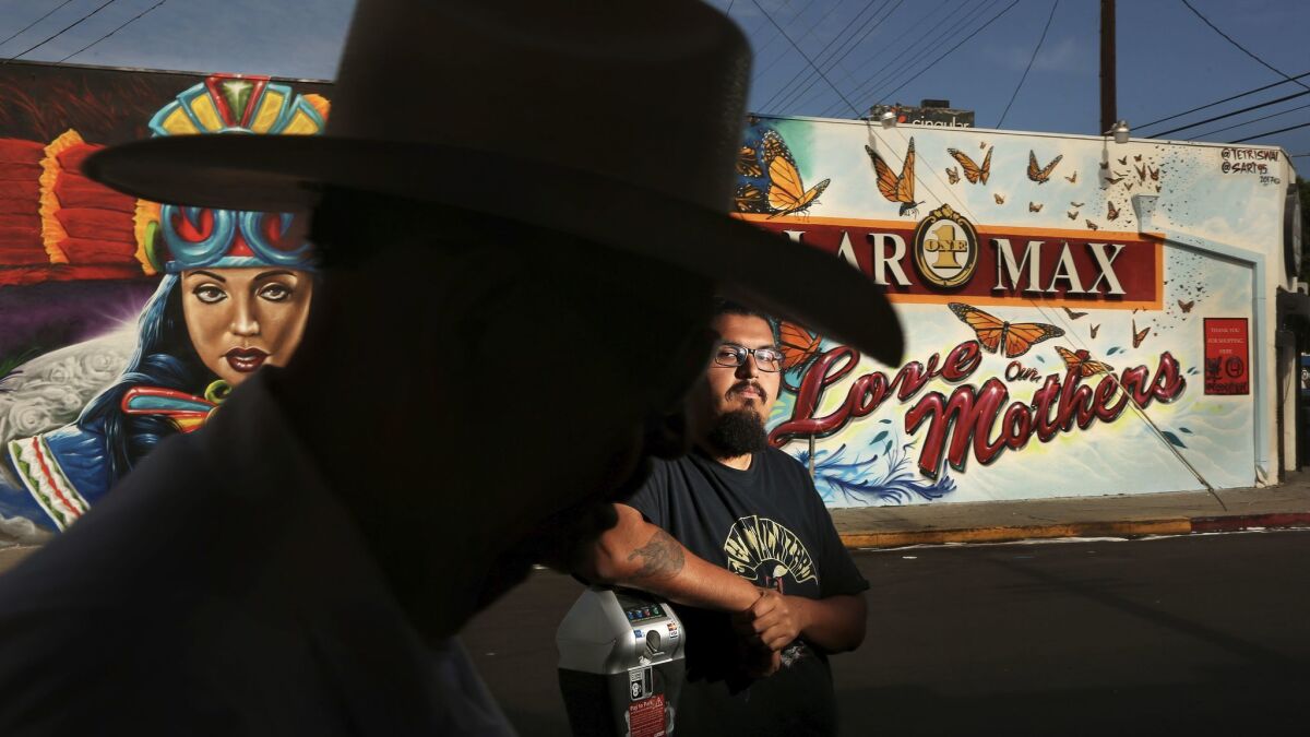 Adrian Ulloa, 21, stands in front of a mural he worked on that was recently completed on the side of a dollar store that runs along Cesar E. Chavez Avenue in the Boyle Heights. The mural is titled "Love our Mothers." (Rick Loomis / Los Angeles Times)