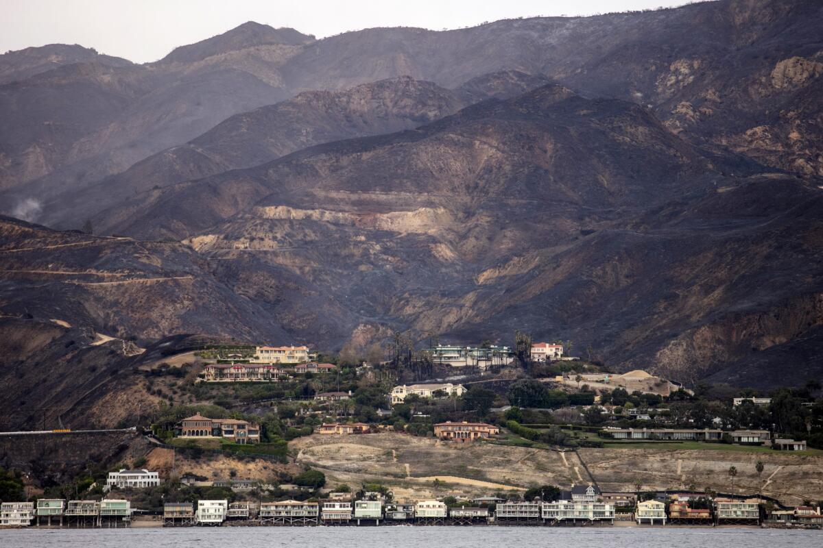 The charred Santa Monica Mountains rise behind homes in Malibu,CA.