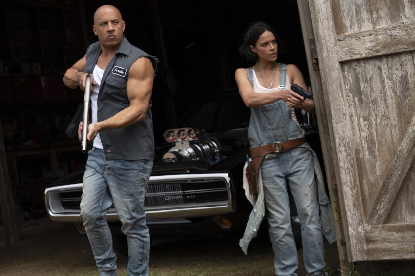  Vin Diesel, in a shirt with ripped off sleeves, and Michelle Rodriguez, in overalls, hold guns by a barn door.