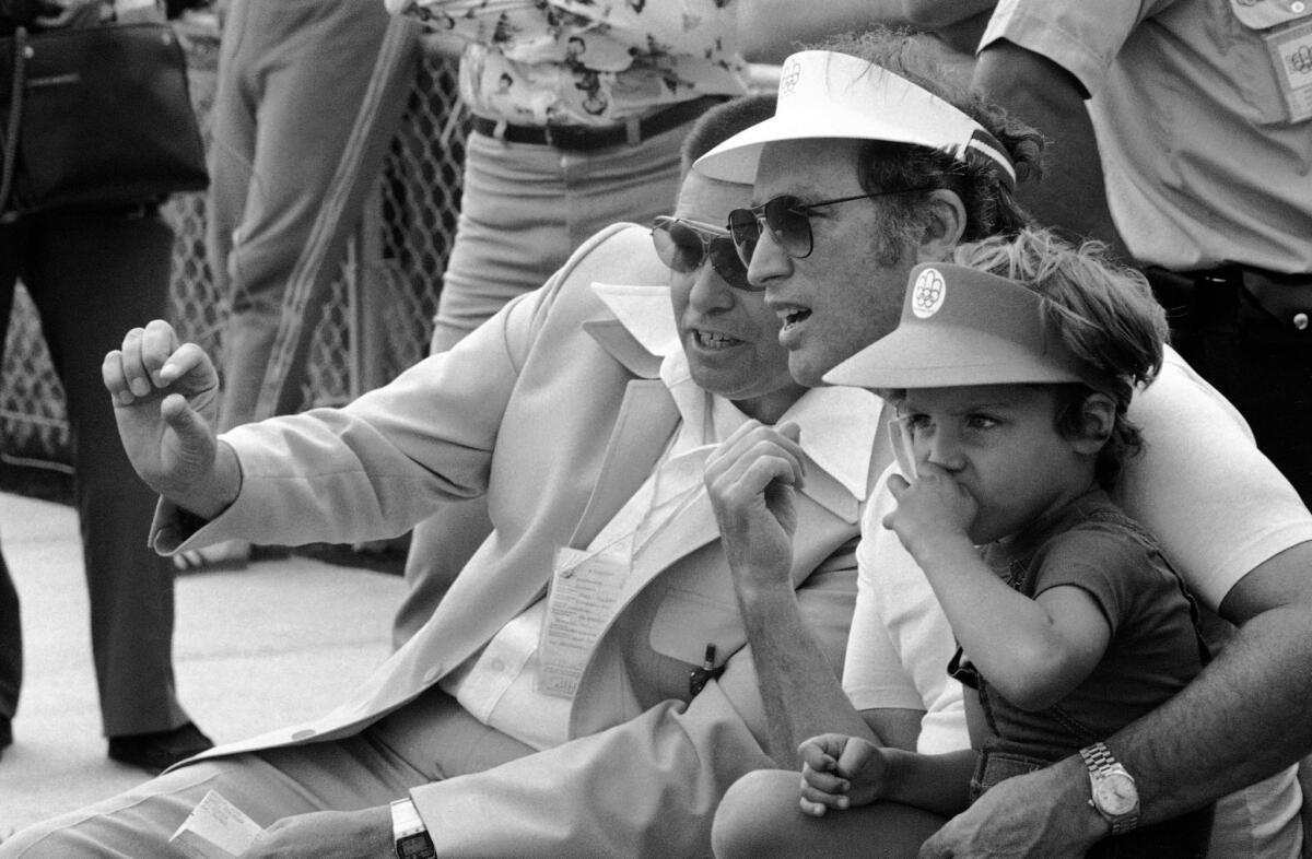 Gil Henderson, left, manager of the Olympic shooting range in Montreal, talks with Canadian Prime Minister Pierre Trudeau, sitting in the stands with his son, Justin, on July 23, 1976.