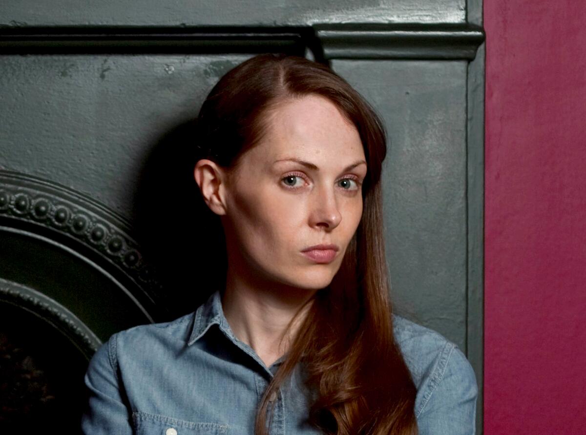 A woman with long hair swept to one side looks seriously at the camera.