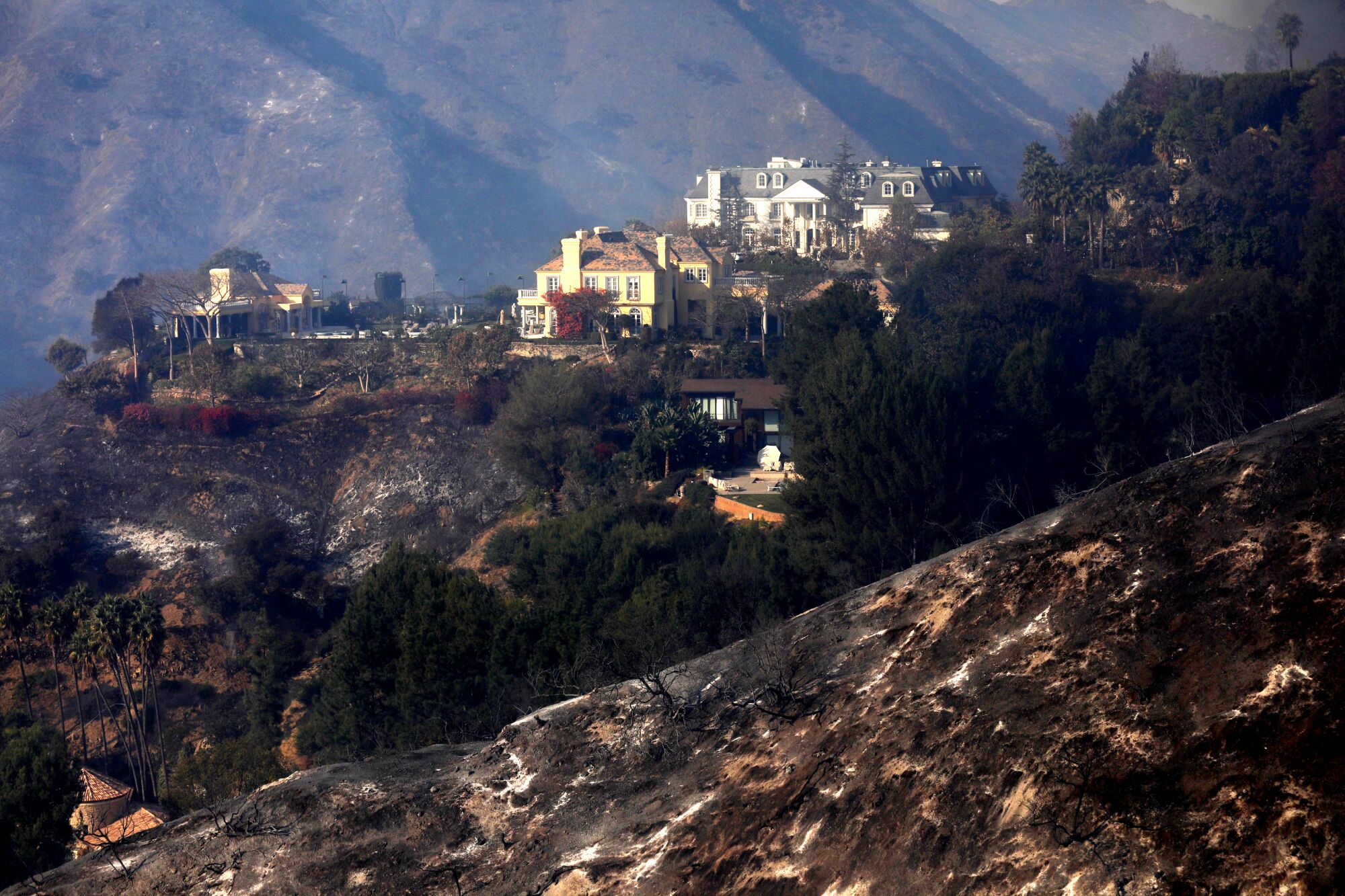 Scorched earth is seen in the foreground, with a group of mansions in the background