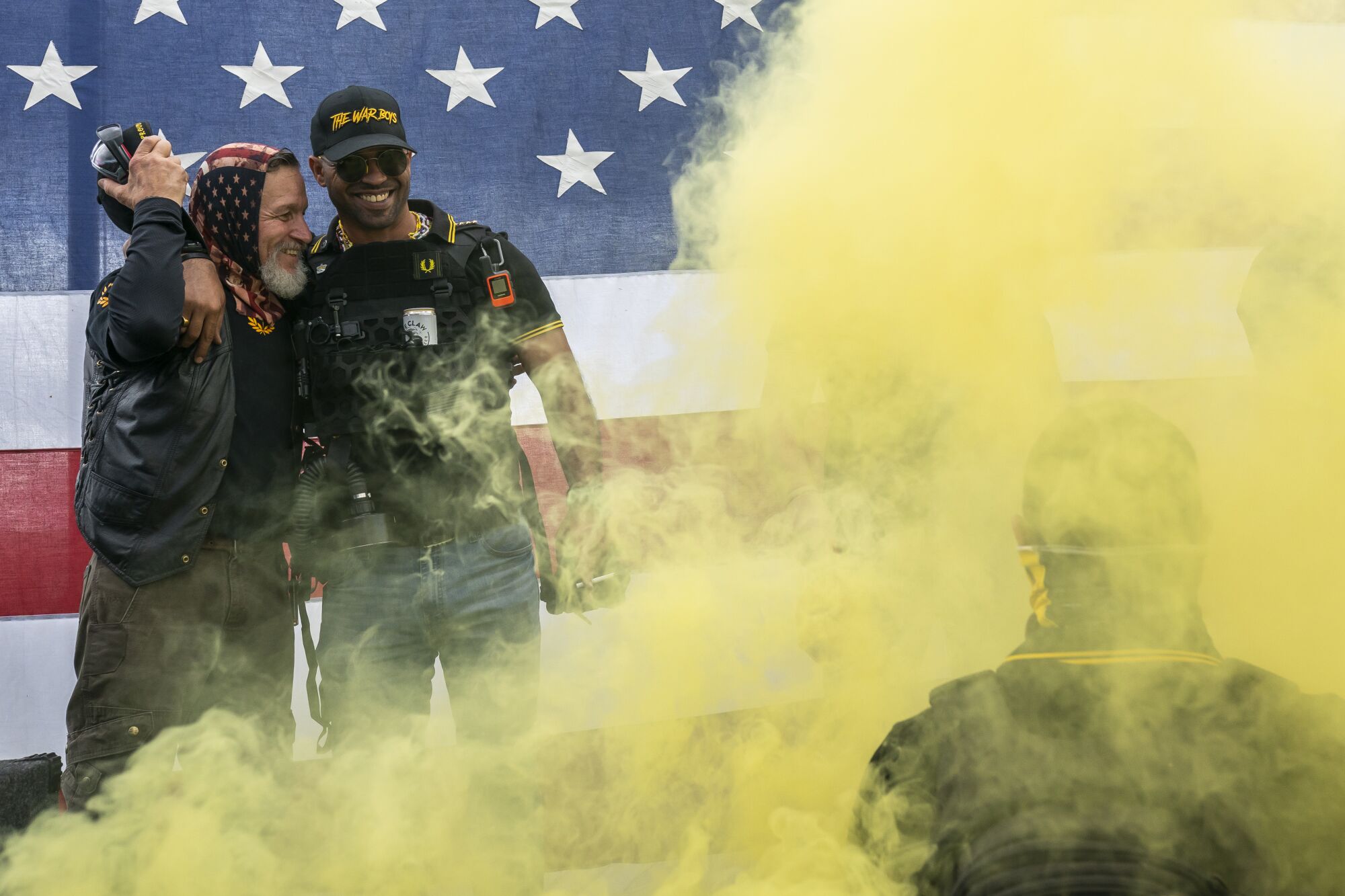 Yellow smoke rises around men in Proud Boys gear in front of a U.S. flag