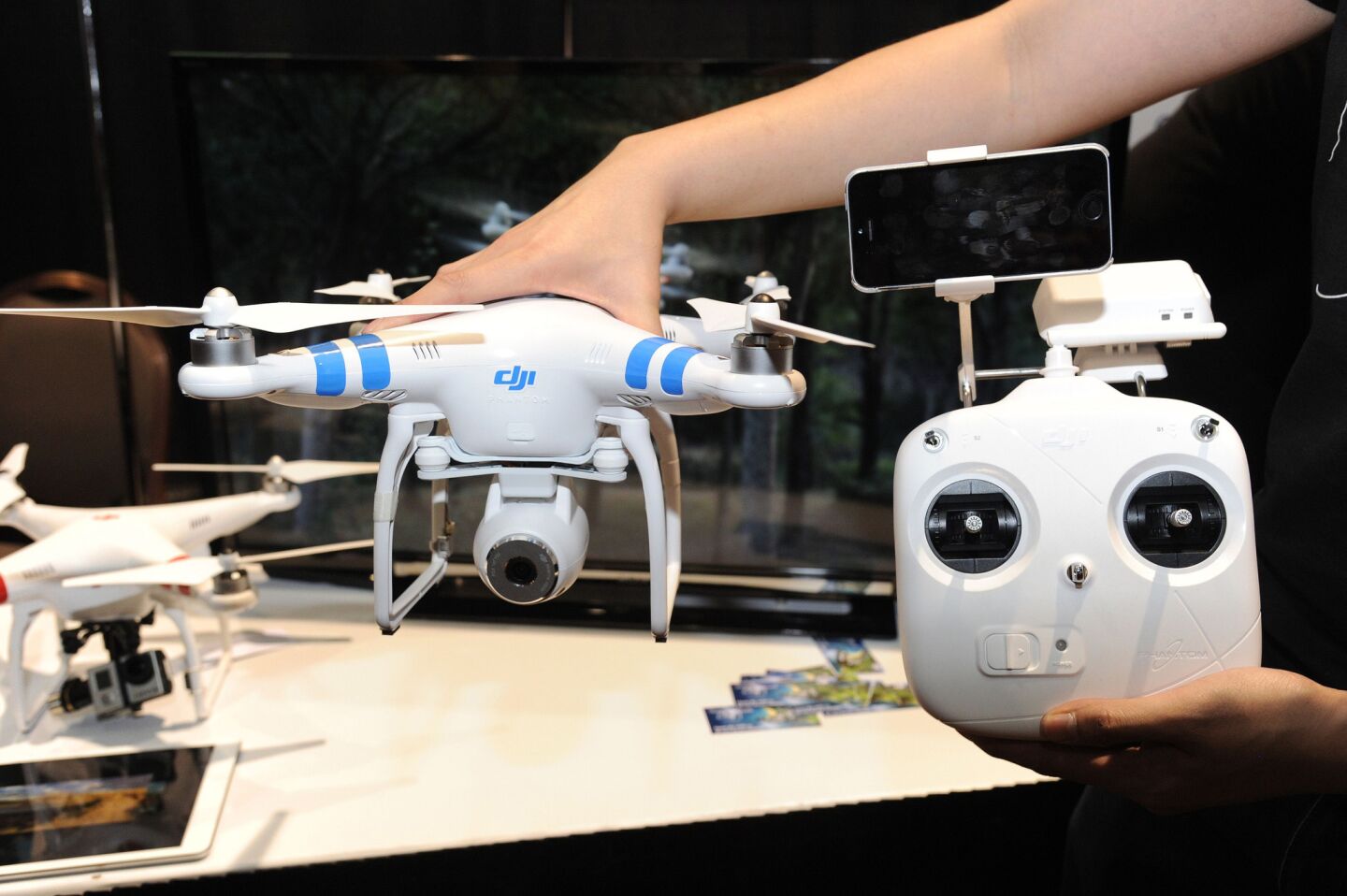 A DJI Innovations DJI Phantom 2 Vision aerial system drone with controller, right, is shown during "CES: Unveiled," the media preview for International CES. The Phantom 2 Vision, available for $1,199, has a 14-megapixel camera on board that can shoot raw photos and 1080p video. The video can be seen live and can be stored on an iPhone or Android smartphone attached to the controller.