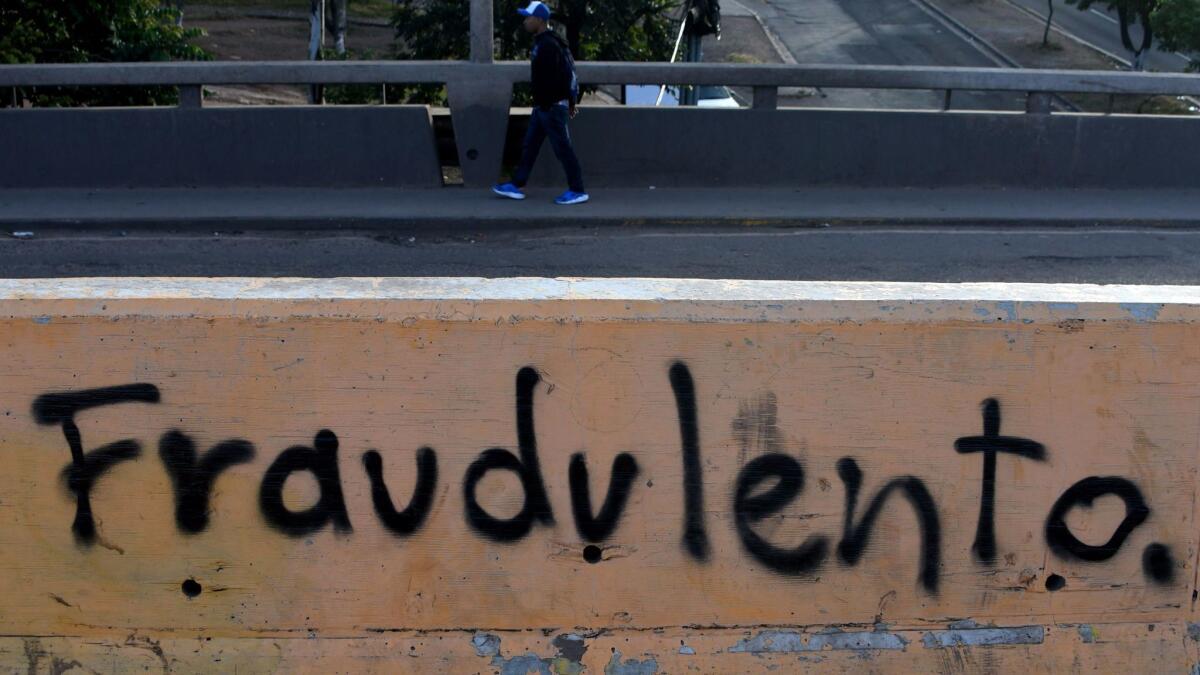 A man crosses a bridge painted with the word "fraudulent" in Tegucigalpa, Honduras, on Sunday, the day after the government declared a state of emergency and imposed a 10-day curfew as concerns rose over election results.
