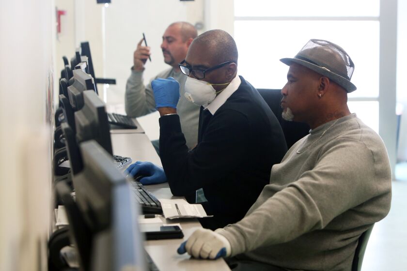 LOS ANGELES, CA-MARCH 26, 2020: Stanley Smith, center, with South L.A. WorkSource Center helps Gregory Allen, right, in the computer lab with job finding services on March 26, 2020 in Los Angeles, California. The number of Americans applying for jobless benefits soared to unprecedented levels last week as new government data put into stark relief the magnitude of the economic pain caused by the coronavirus outbreak. (Photo By Dania Maxwell / Los Angeles Times)