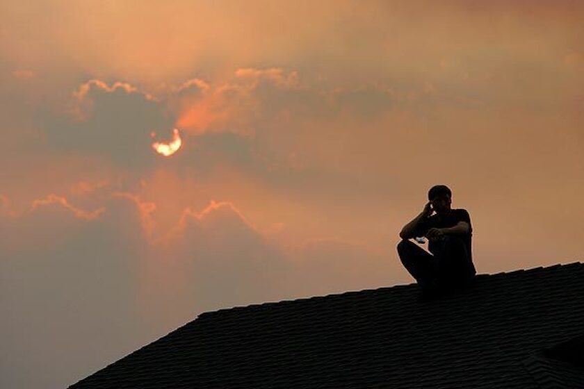 A resident sits on his roof to watch the Station fire burn in a canyon near homes off Boston Avenue in La Crescenta.