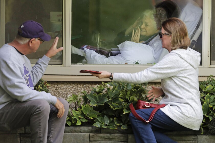 FILE - In this March 11, 2020, file photo Judie Shape, center, who has tested positive for the coronavirus, blows a kiss to her son-in-law, Michael Spencer, left, as Shape's daughter, Lori Spencer, right, looks on, as they visit on the phone and look at each other through a window at the Life Care Center in Kirkland, Wash., near Seattle. Nursing home residents vaccinated against COVID-19 can get hugs again from their loved ones, and indoor visits may be allowed for all residents, the government said Wednesday, March 10, 2021 in a step toward pre-pandemic normalcy (AP Photo/Ted S. Warren, File)