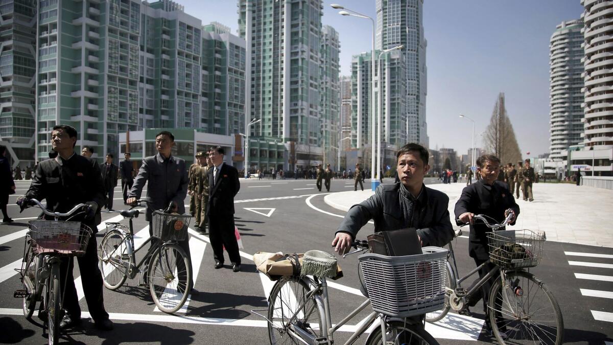 North Korean men push their bicycles along Ryomyong residential area, a collection of more than a dozen new apartment buildings in Pyongyang,