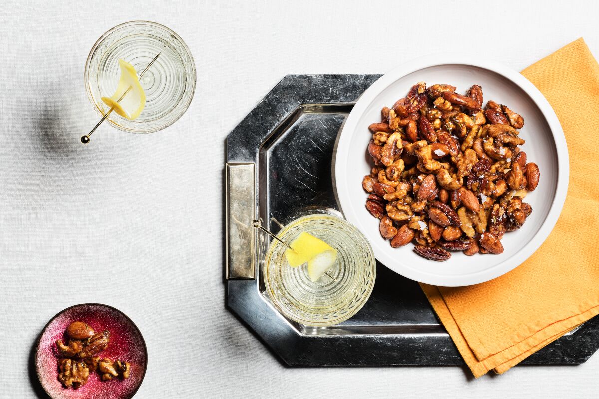 A bowl of mixed nuts with glasses of clear liquid.