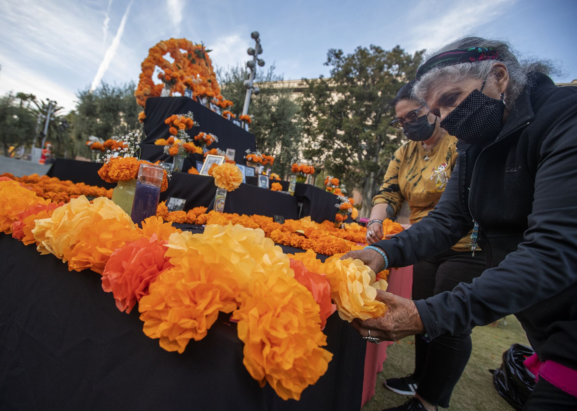 Two women place paper marigolds on a community Day of the Dead altar.
